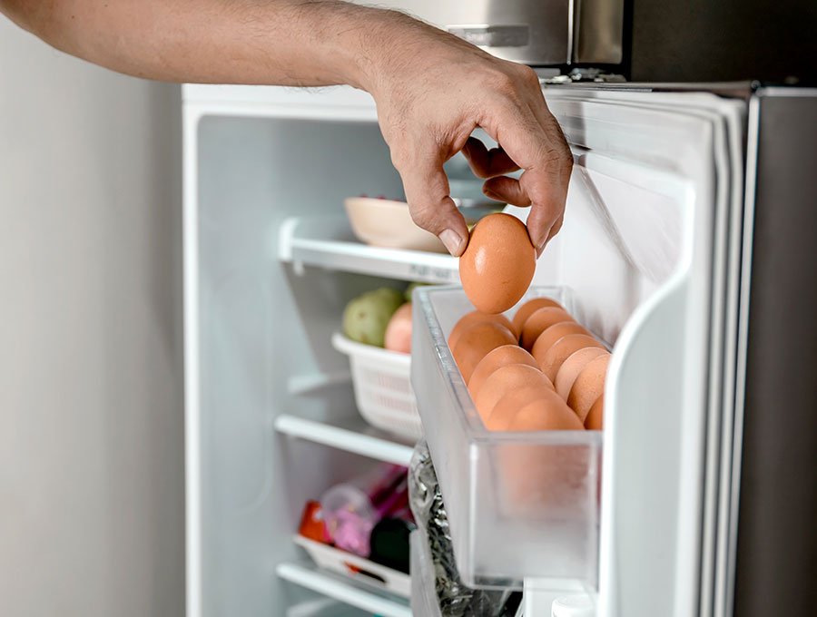 Este hombre está cogiendo un huevo del interior del mini frigorífico de la cocina.