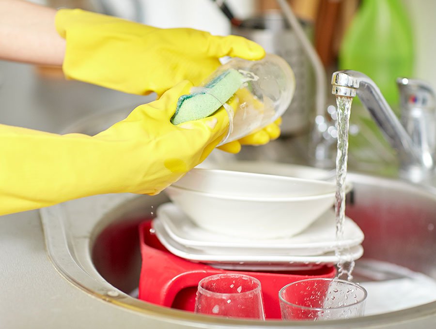 Esta mujer limpia los vasos y platos en el fregadero.