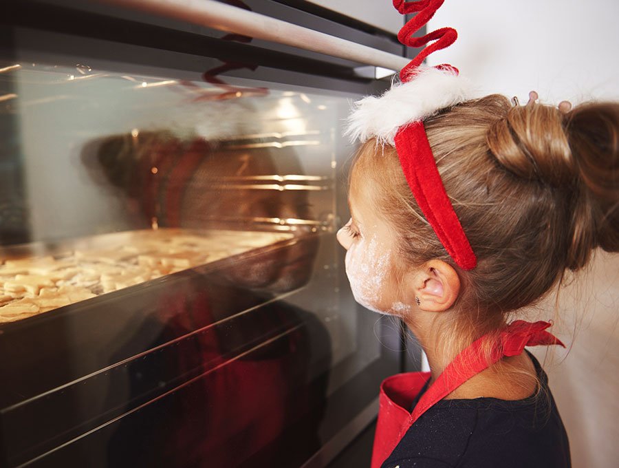 Esta niña con harina en la cara está mirando cómo se cocinan las galletas en el horno.
