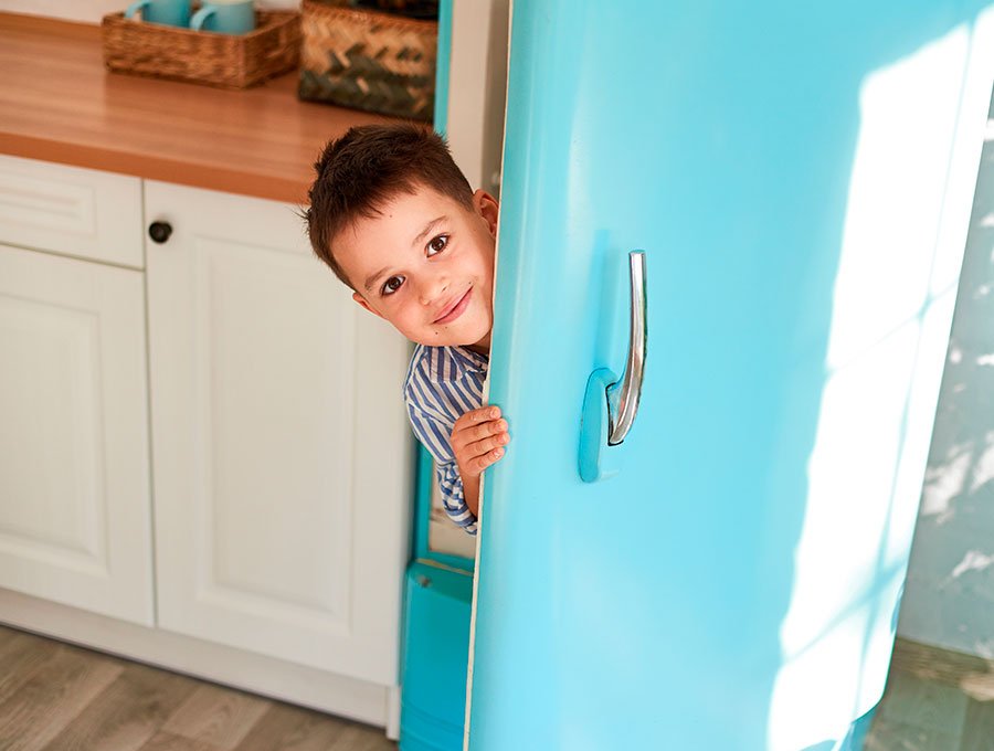 Niño pequeño se esconde tras la puerta del frigorifico de color azul.