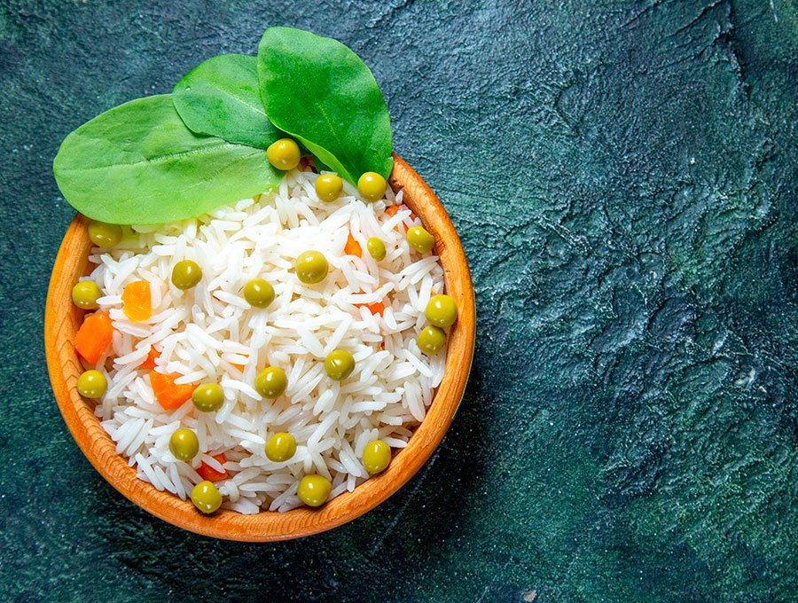 Un plato pequeño lleno de arroz cocido con guisantes y pimientos rojos.