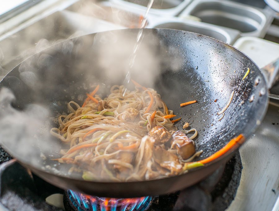 Un chef está preparando unos tallarines salteados con carne y verduras en el wok.