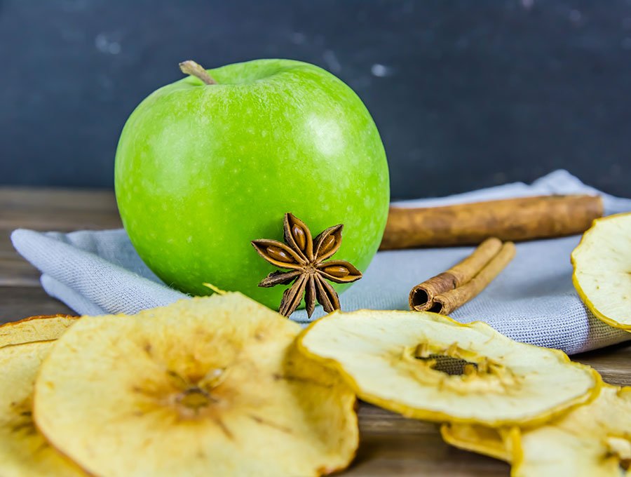 Rodajas de manzana deshidratada junto a una manzana verde natural.